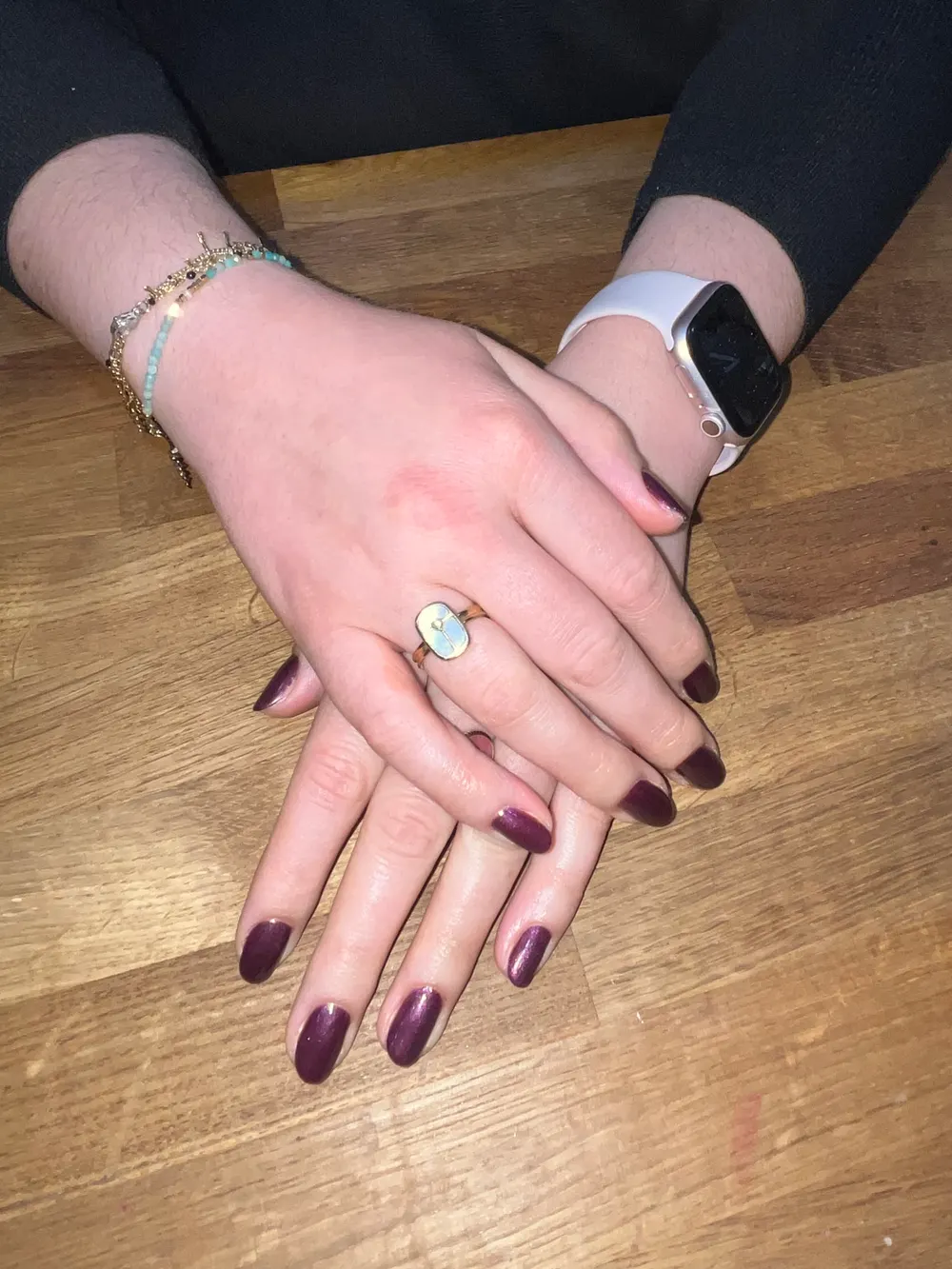 Mains croisées sur la table en chêne du salon, ongles semi-permanent bordeaux nacré