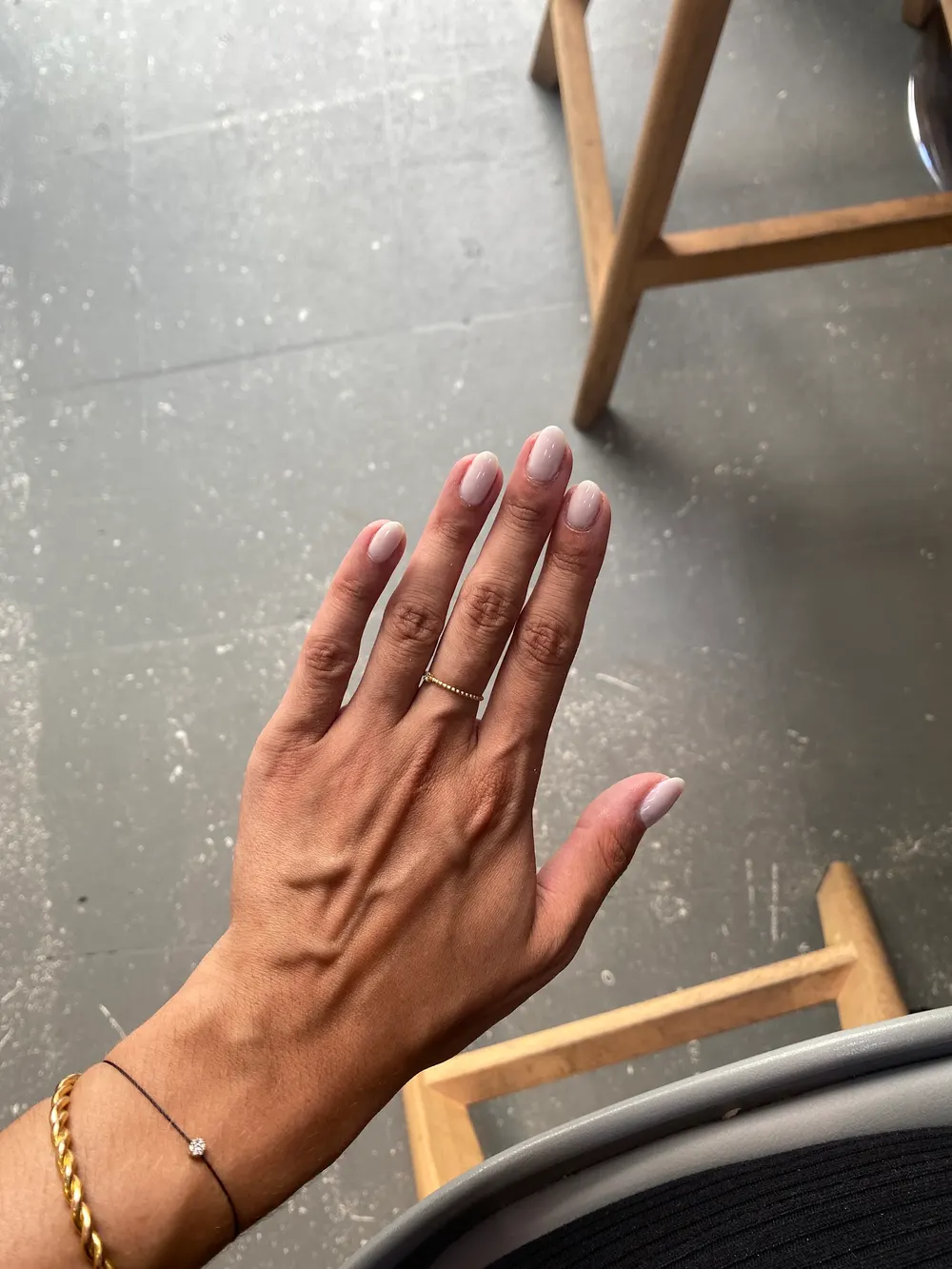 Main ouverte aux ongles rose lacté au-dessus du sol gris du salon